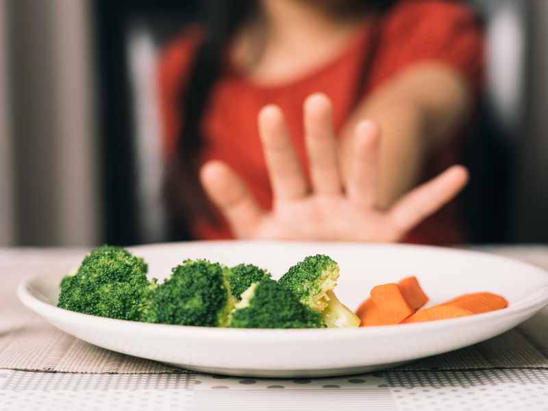 A kid pushing a plate of food away
