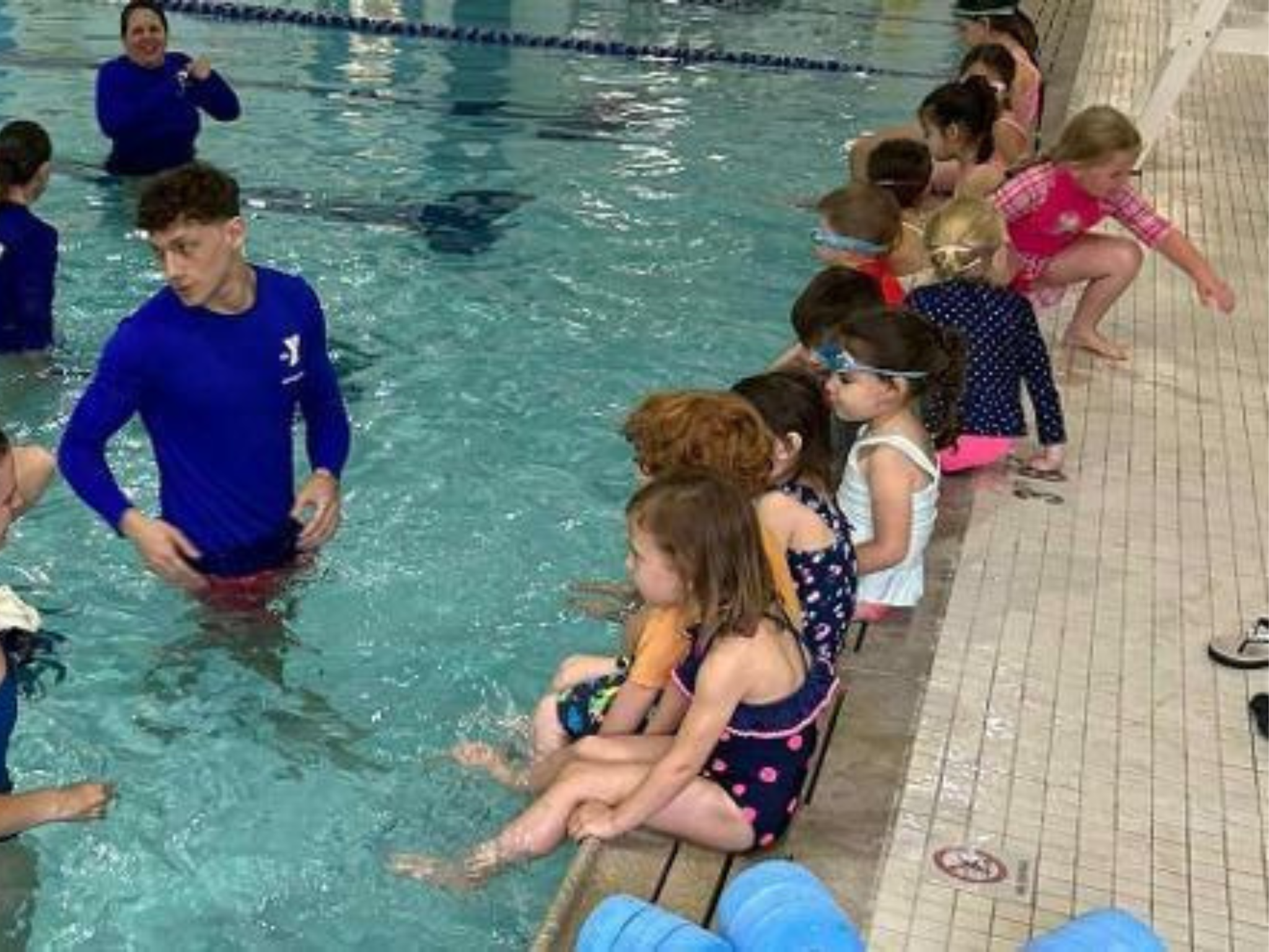 Kids sitting at the edge of the pool listening to their Safety Around Water instructor at the YMCA