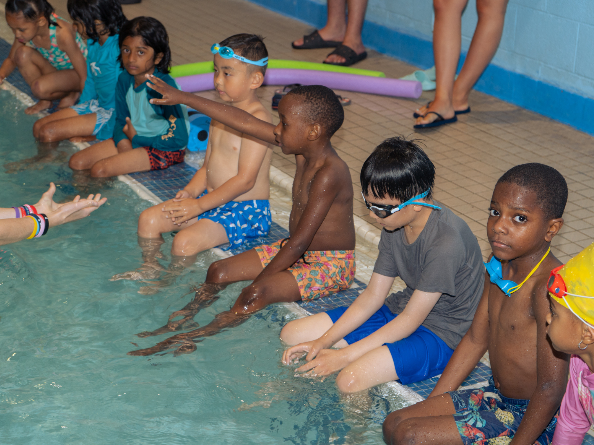 Kids sitting at the edge of the pool waiting for instruction during Safety Around Water class