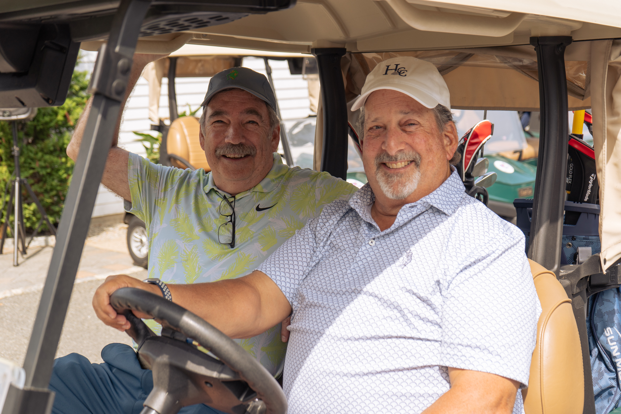 Two men riding in a golf cart at the Sussex County YMCA Golf Outing